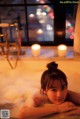 A woman laying in a bathtub with candles in the background.