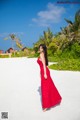 A woman in a red dress standing on a white sand beach.