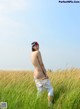 A naked woman standing in a field of tall grass.